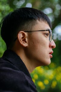 Close-up side profile of a young man with eyeglasses in a natural outdoor setting.